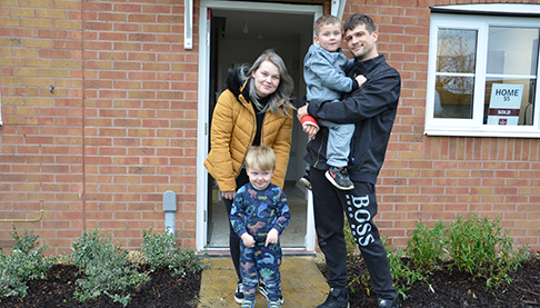 Happy family of mum dad and two young boys stood outside their new home.