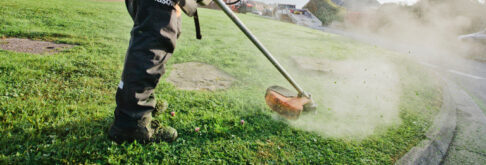 Grounds maintenance worker using a strimmer to cut grass on a verge