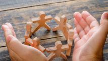 Wooden people figures being protected by human hands