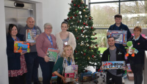 Team members holding gifts and smiling in front of a Christmas tree.