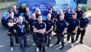 Two Rivers Housing repairs team in matching blue uniforms stood in front of Two Rivers Housing van with the words You're Home Now