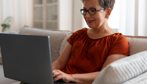 Woman sat on her sofa using a laptop to access information.